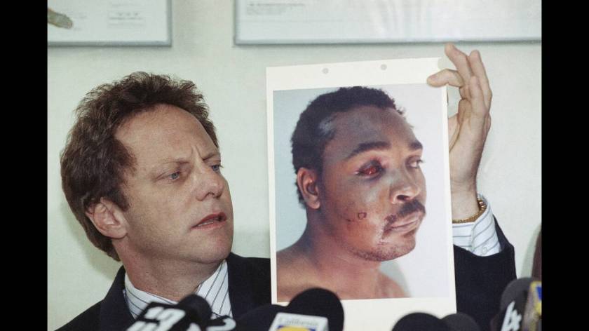 1991
Ο δικηγόρος του Ρόντνεϊ Κινγκ παρουσιάζει σε συνέντευξη Τύπου μια φωτογραφία του πελάτη του, ο οποίος ξυλοκοπήθηκε άγρια και εντελώς αναίτια από λευκούς αστυνομικούς μετά από μια τροχαία παράβαση. η δίκη του Κινγκ έγινε σύμβολο ενάντια στην αστυνομι